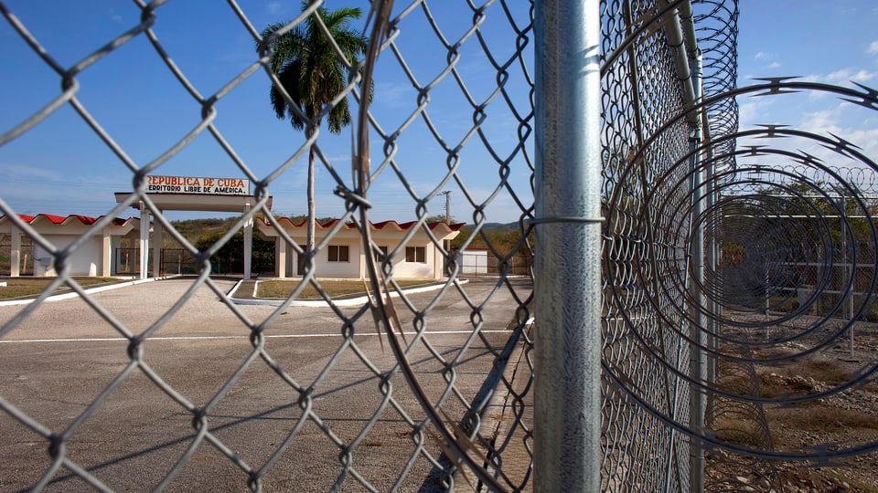 Blick durch hohen Zaun und Stacheldraht ins Gefaengnis Guantanamo