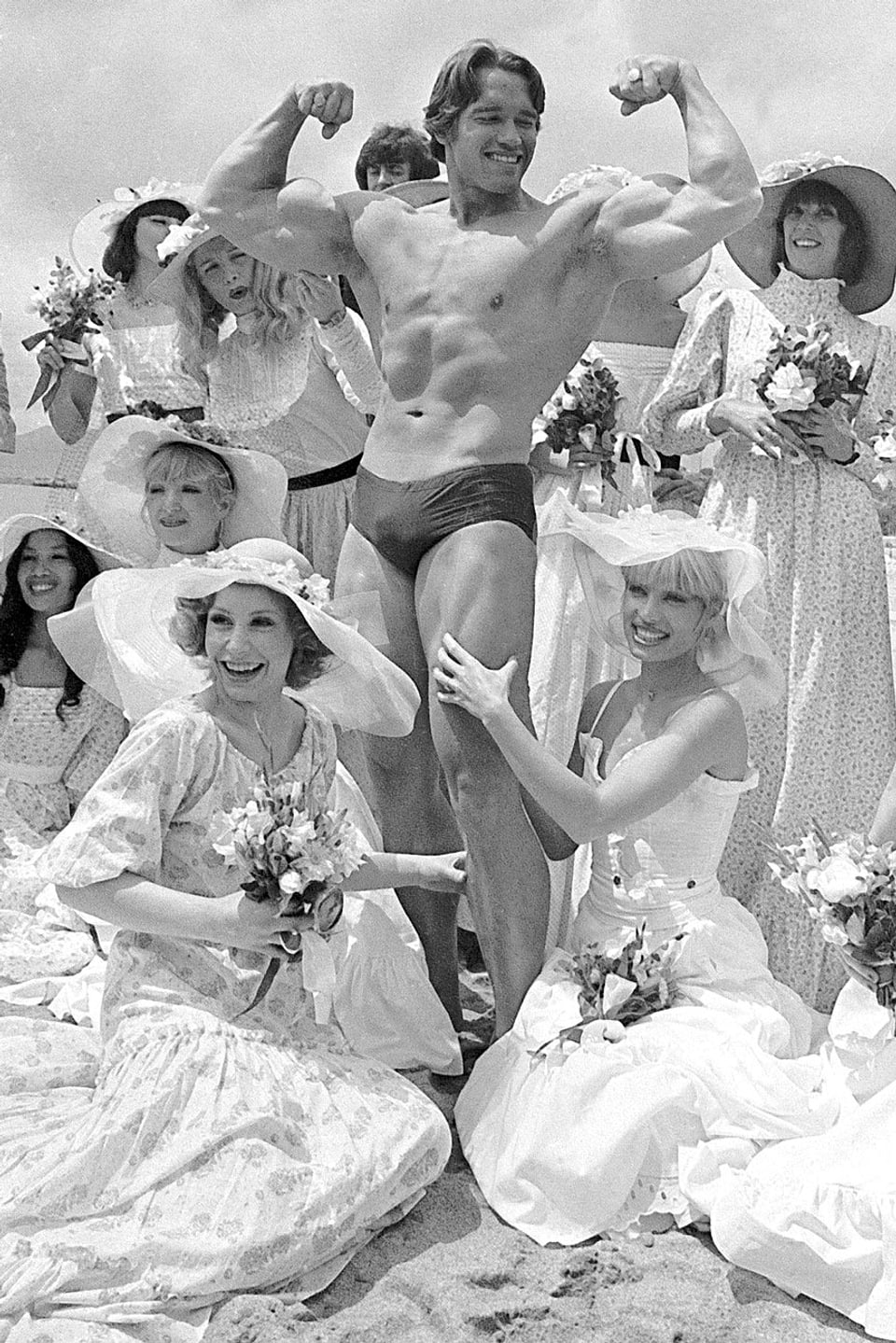 Mann in Bodybuilderpose umgeben von Frauen in langen Kleidern.