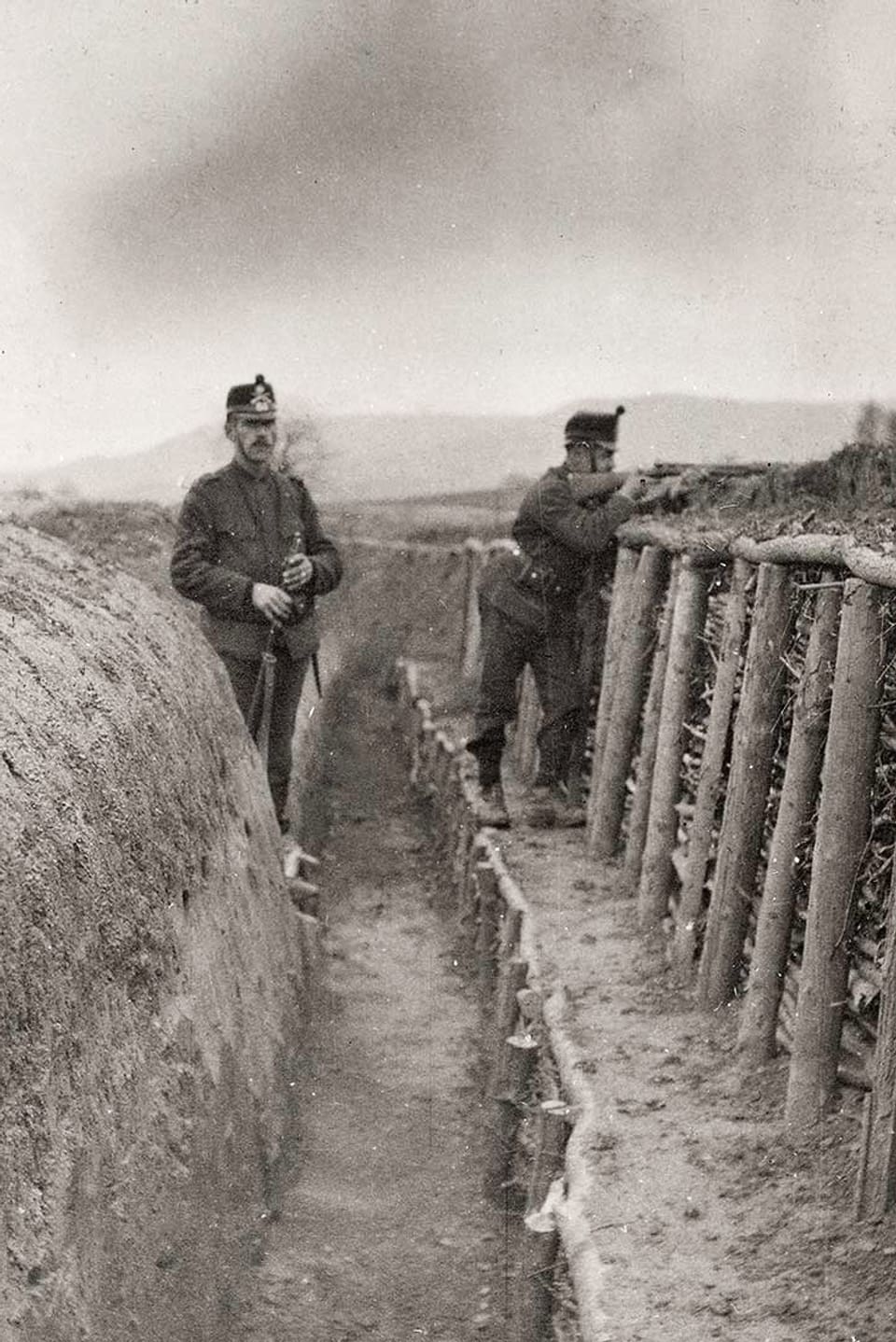 Zwei Soldaten stehen in einem Infanteriegraben. Einer zielt mit einer Waffe.