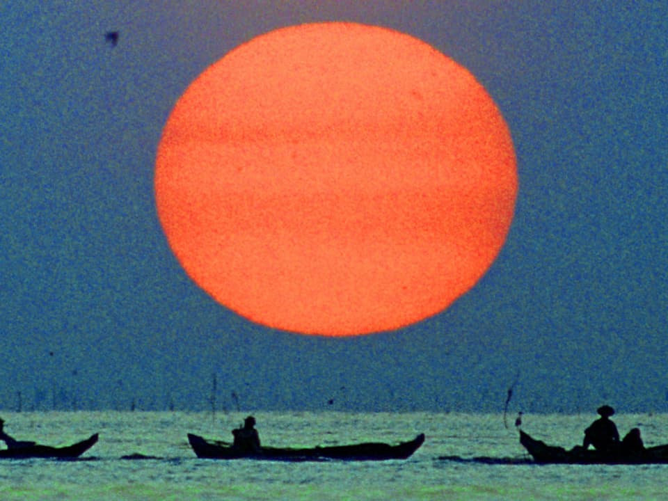Fischerboote auf See, dahinter riesige Abendsonne