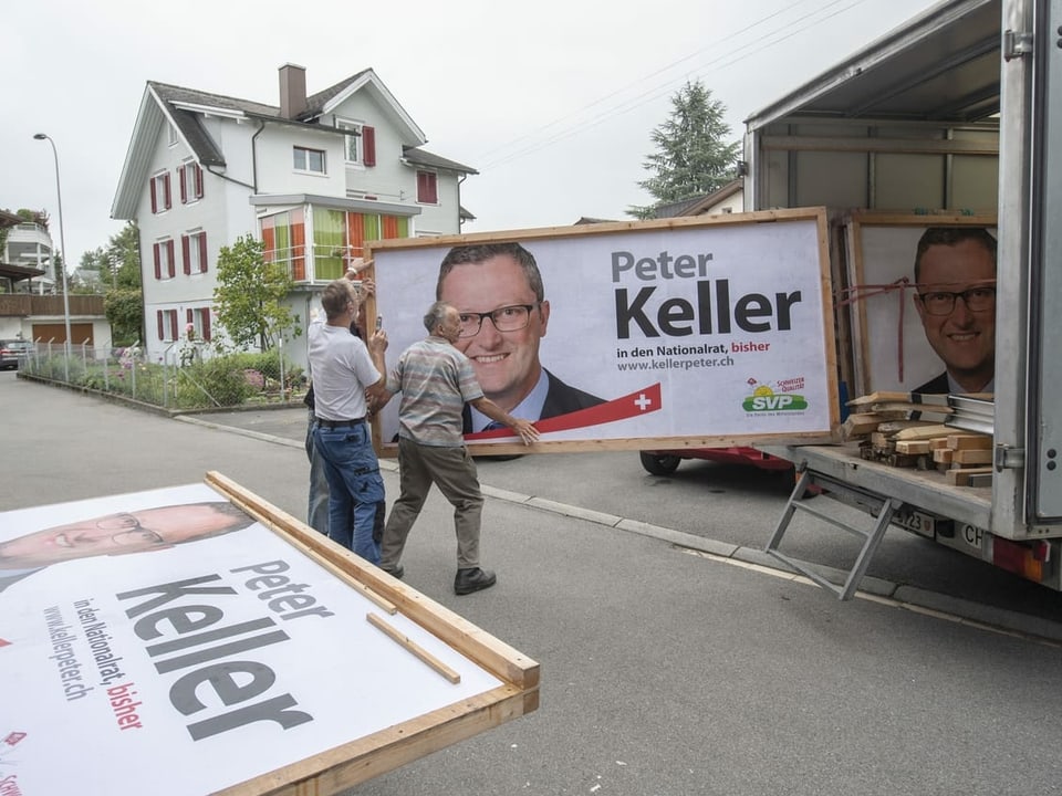 Drei Männer tragen ein grosses Plakat mit der Aufschrift "Peter Keller".