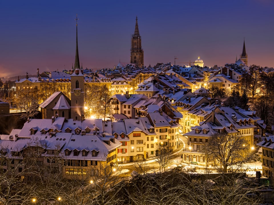 Nacht über der Stadt Bern. Die Lichter der Strassen und Weihnachtsbeleuchtung zaubern eine schöne Atmorphäre. Alles ist frisch verschneit. 