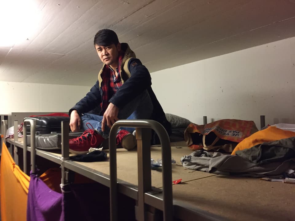 Nazari Juma Khan sitzt auf seinem Bett unter der Decke in der Asylunterkunft. 