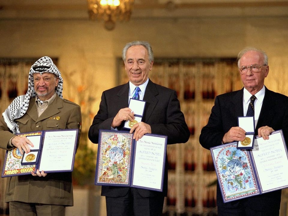 Arafat, Peres und Rabin halten ihre Nobelpreis-Urkunden in die Kamera