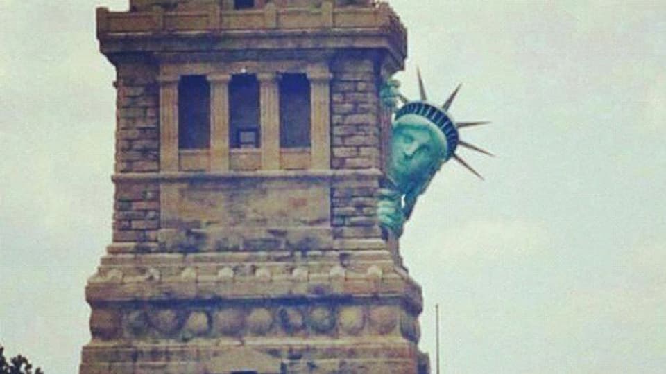 In einer Bildmontage versteckt sich die Freiheitsstatue vor Hurrikan Sandy hinter ihrem Sockel.