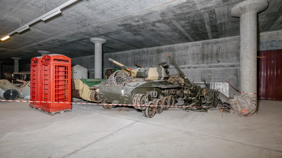 Ein Panzer und alte Telefonkabinen in einem Kellergeschoss.