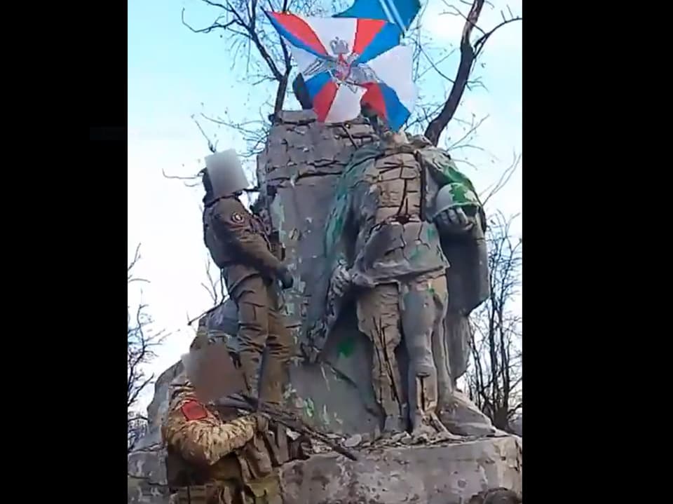 Bewaffnete russische montieren die russische Flagge über einer Statue. 