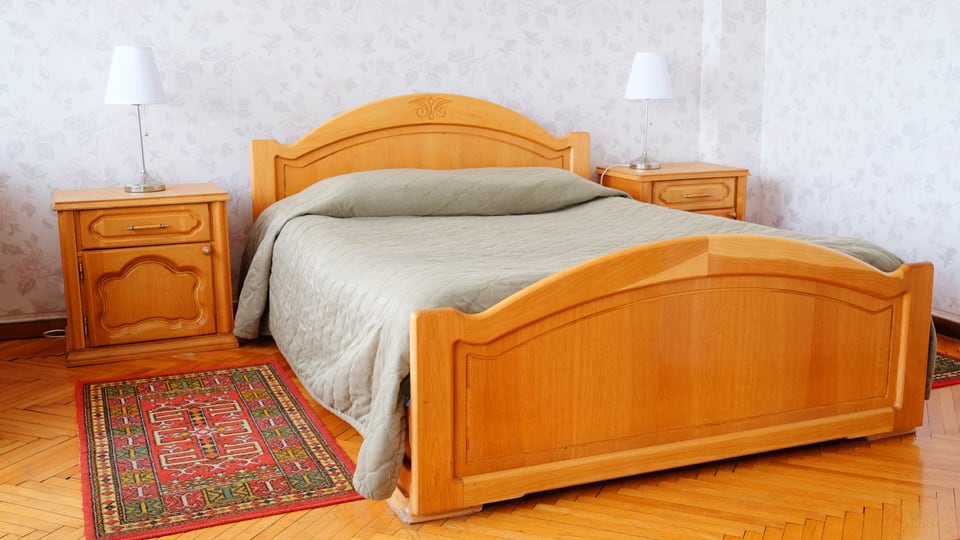 Ein Hotelbett aus Holz, mit Nachttisch und Teppich.