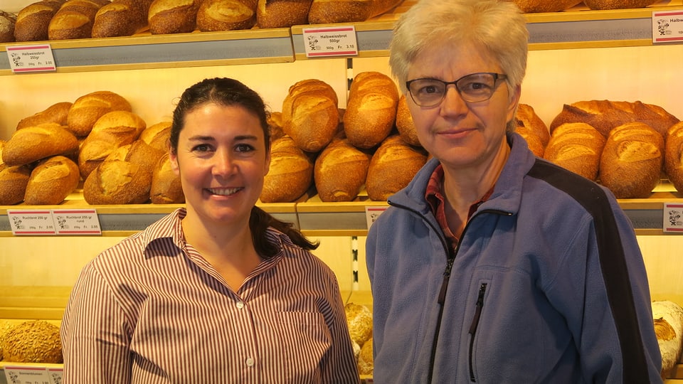Zwei Frauen stehen vor einer Wand mit Broten.