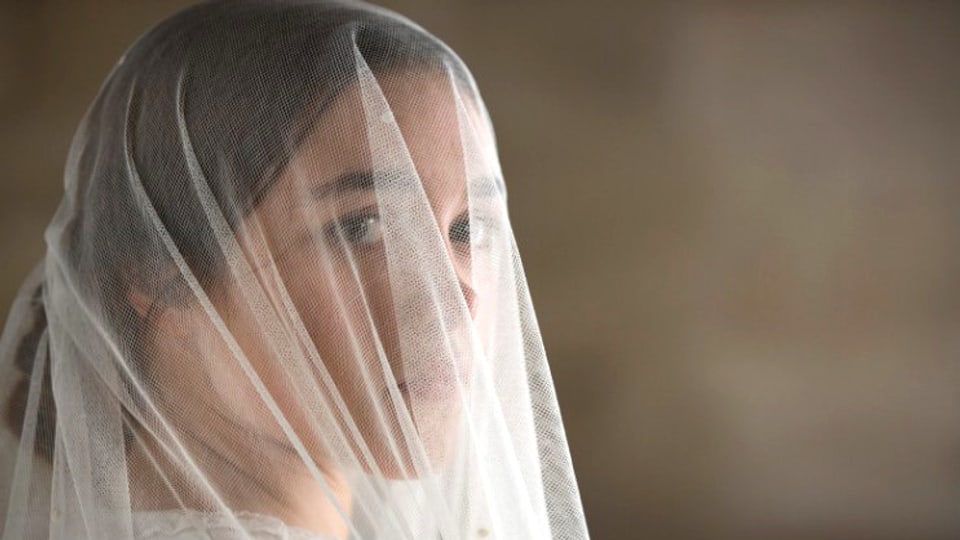 Eine junge Frau, deren Gesicht hinter einem weissen Schleier aufscheint.