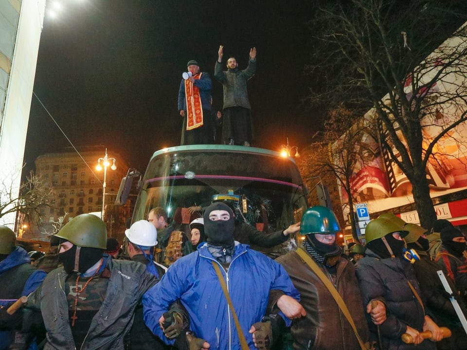 Vermummte Aktivisten formieren sich vor einem Bus, in dem sich gefangen genommene Polizisten aufhalten.