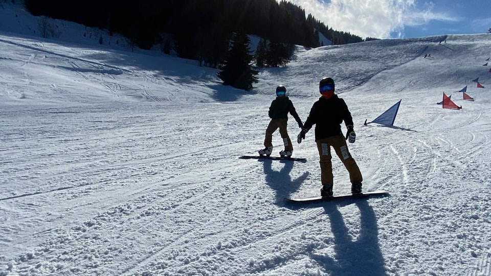 Gaël und sein Kollege stehen auf dem Snowboard im Schnee. Sie fahren langsam von Tor zu Tor.