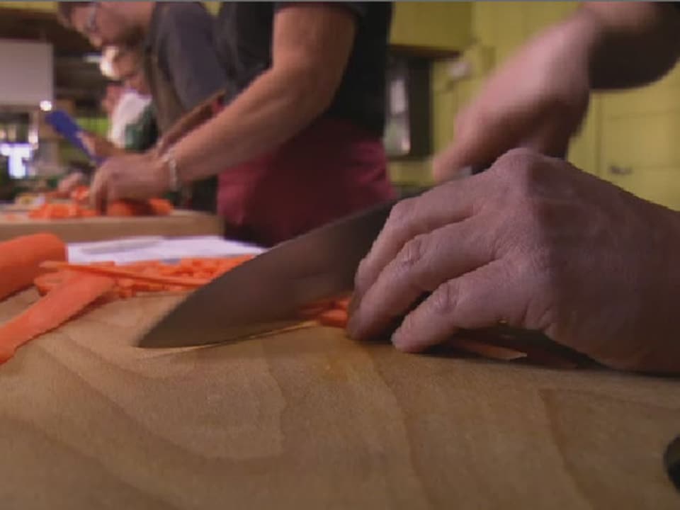 Mann schneidet auf einem Holzbrett Karotten.