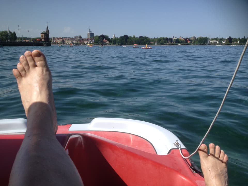 Jemand sitzt auf einem Boot und streckt die Füsse zur Abkühlung in den Bodensee.