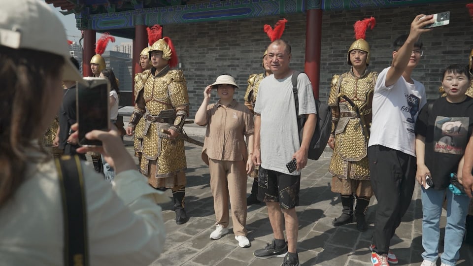 A man stands next to masked soldiers with a red feather on their heads.