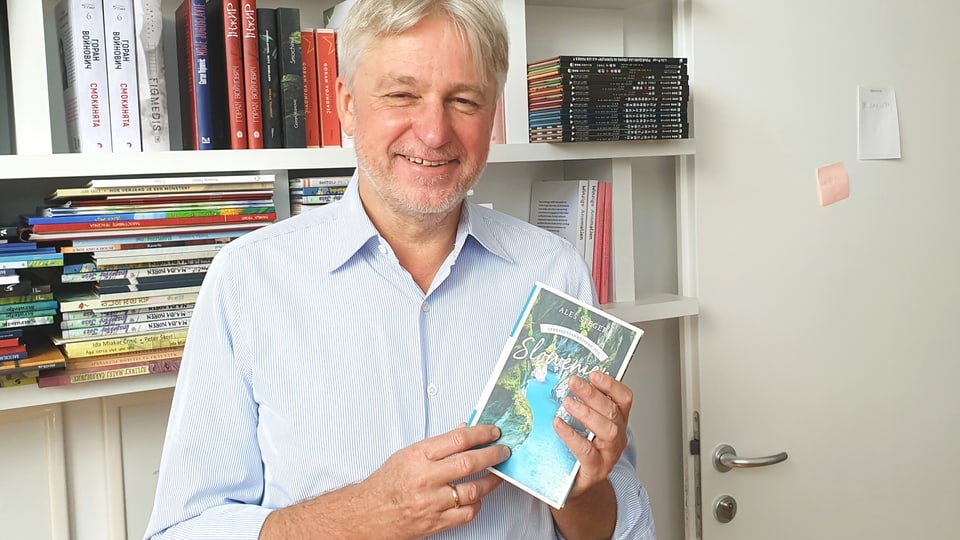 Man with white hair and a stubble holds a book in his hands