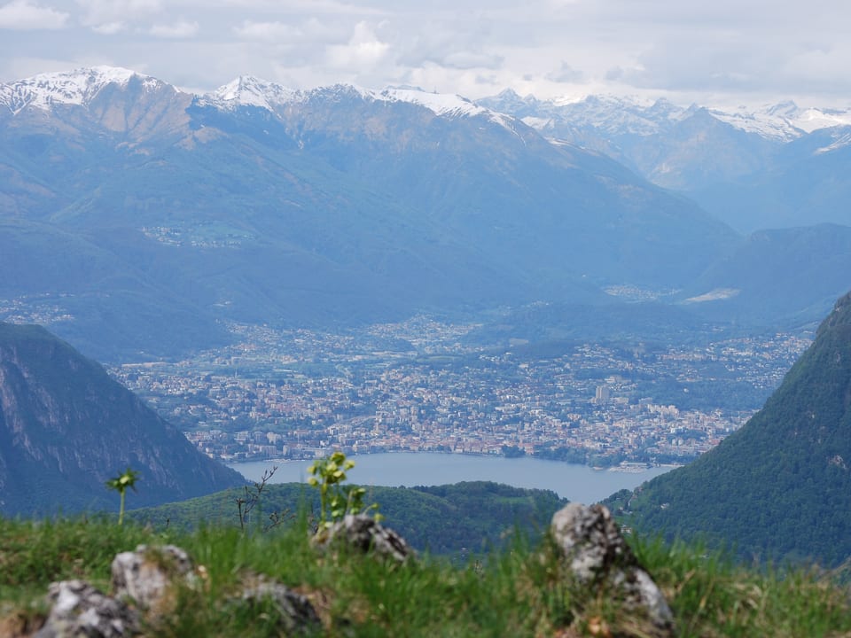 Panoramafoto vom Berg mit Blick auf See, Stadt Lugano und schneebedeckte Gipfel im Hintergrund. 