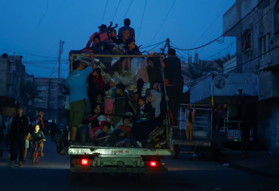 Menschen auf einem überfüllten Lastwagen unterwegs in der Dämmerung in einer städtischen Umgebung.