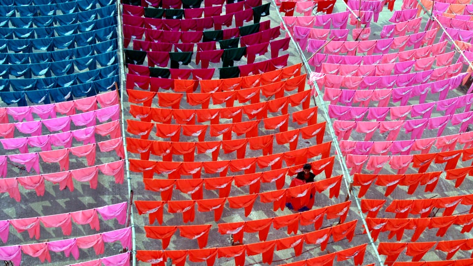 Ein Arbeiter hängt verschieden gefärbte Kleidung zum Trocknen auf eine Leine.
