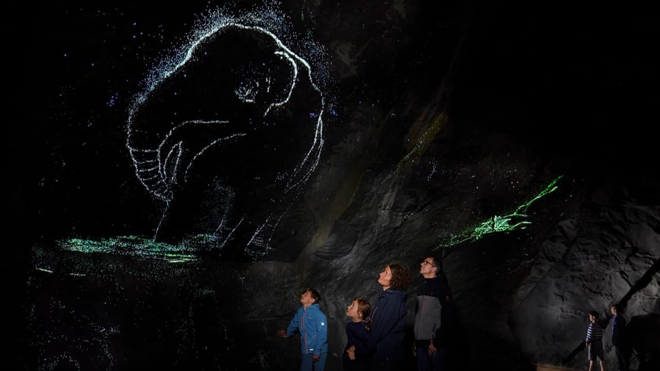 Eine Familie betrachtet ein Lichtspiel eines Mammuts an einem Felsen.