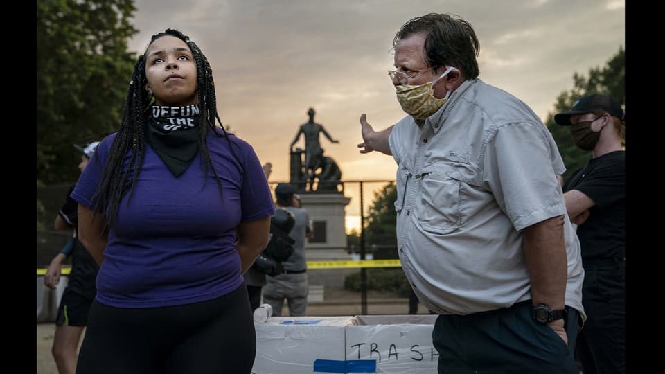 Ein Mann mit Bauch redet auf eine junge schwarze Frau ein.