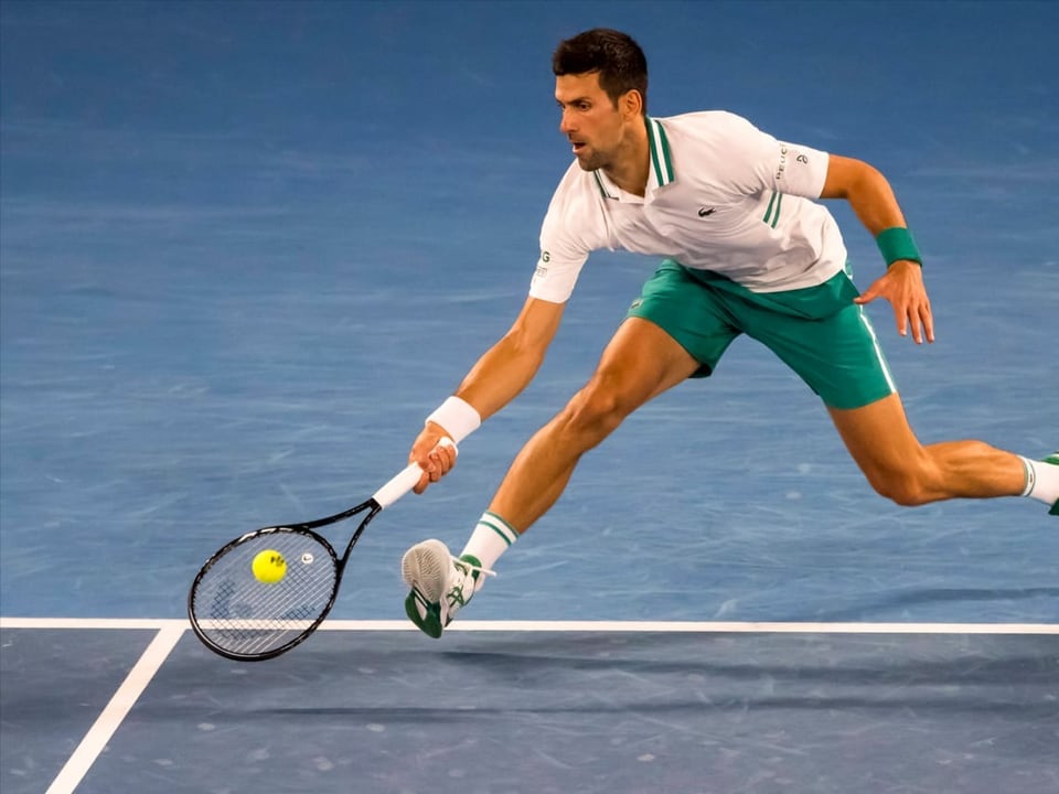 Novak Djokovic schlägt einen Ball nahe am Boden.