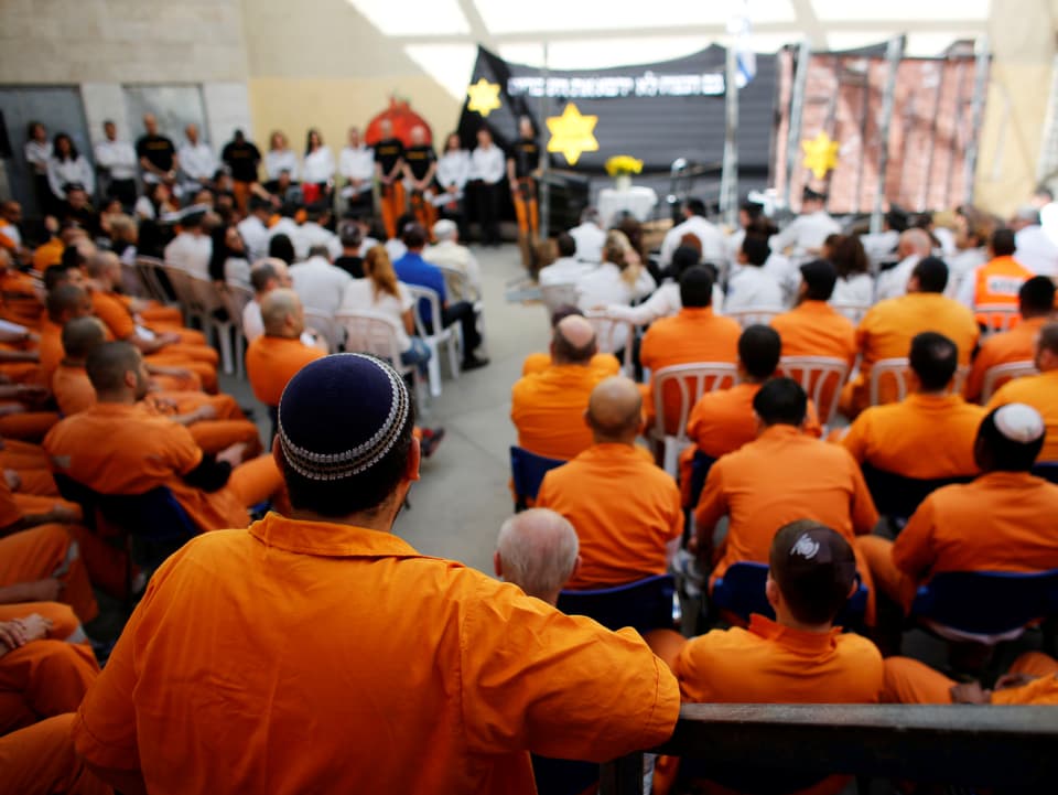 Orange gekleidete Häftlinge bei einer Gedenkfeier.
