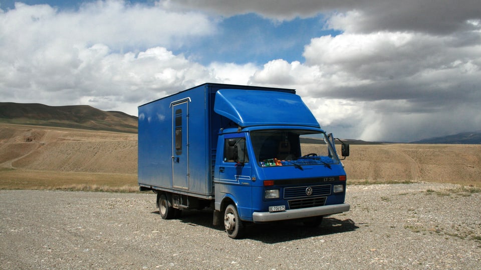 Ein blauer, umgebauter VW-Bus vor hügeliger Landschaft.