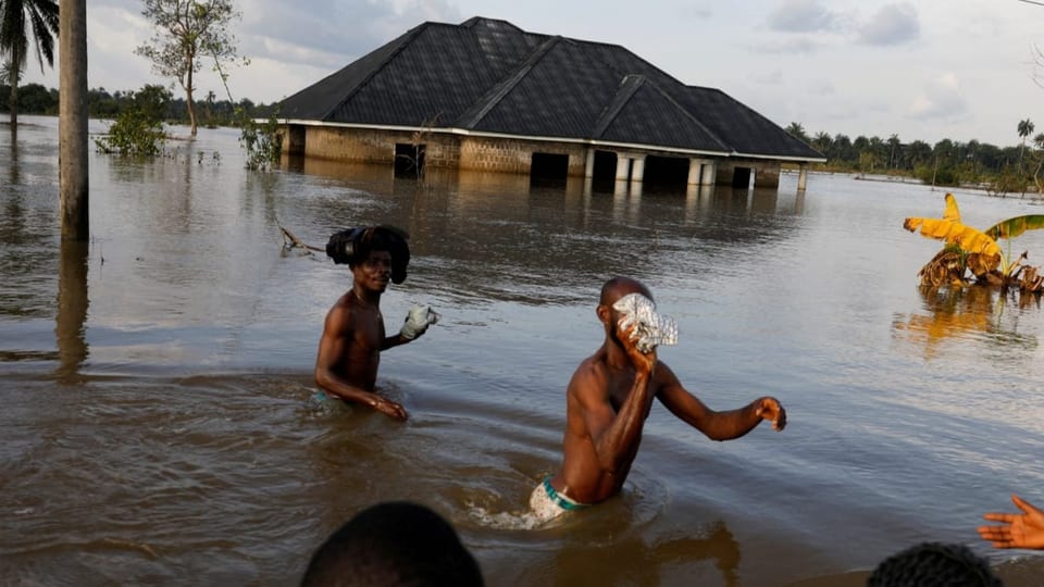 Zwei Jugendliche sind hüfthoch im Wasser. Im Hintergrund ein Haus, zur Hälft unter Wasser. Bilder aus Nigeria.