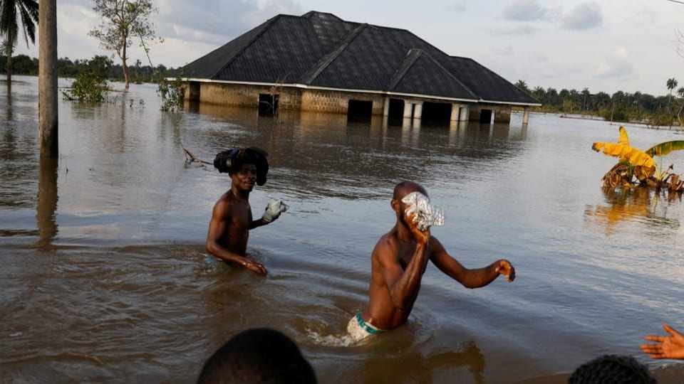 Zwei Jugendliche sind hüfthoch im Wasser. Im Hintergrund ein Haus, zur Hälft unter Wasser. Bilder aus Nigeria.