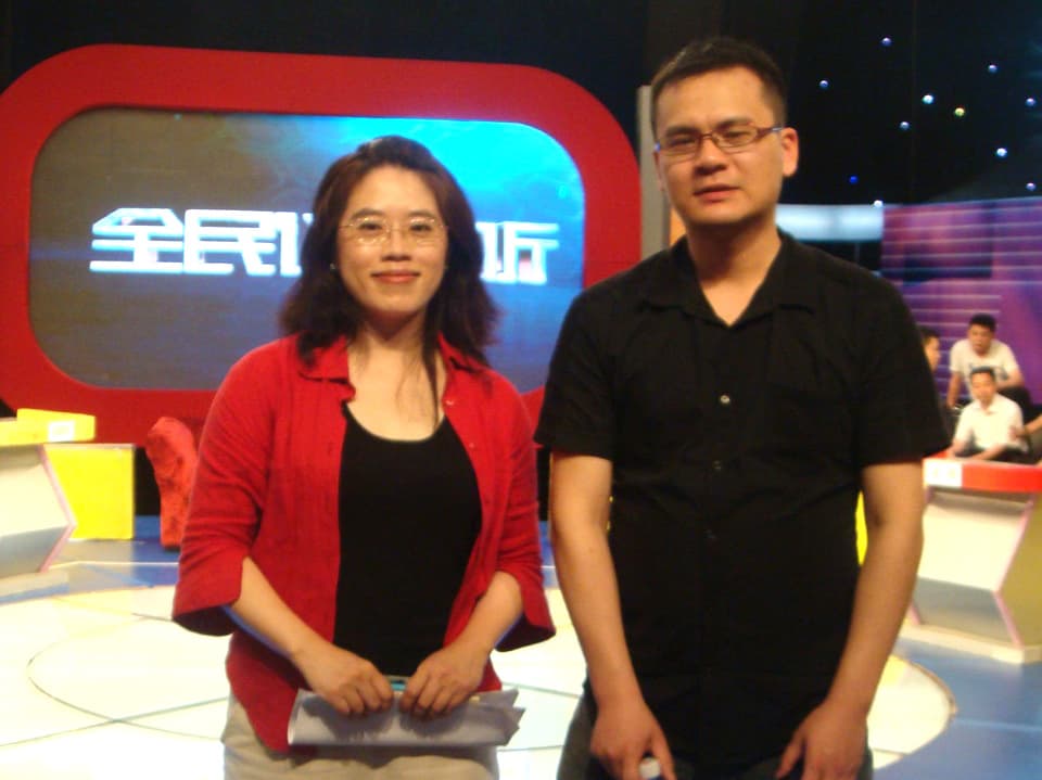 Eine Frau und ein Mann stehen in einem TV-Studio, hinter ihnen ist eine grosser rotgerahmter Bildschirm.