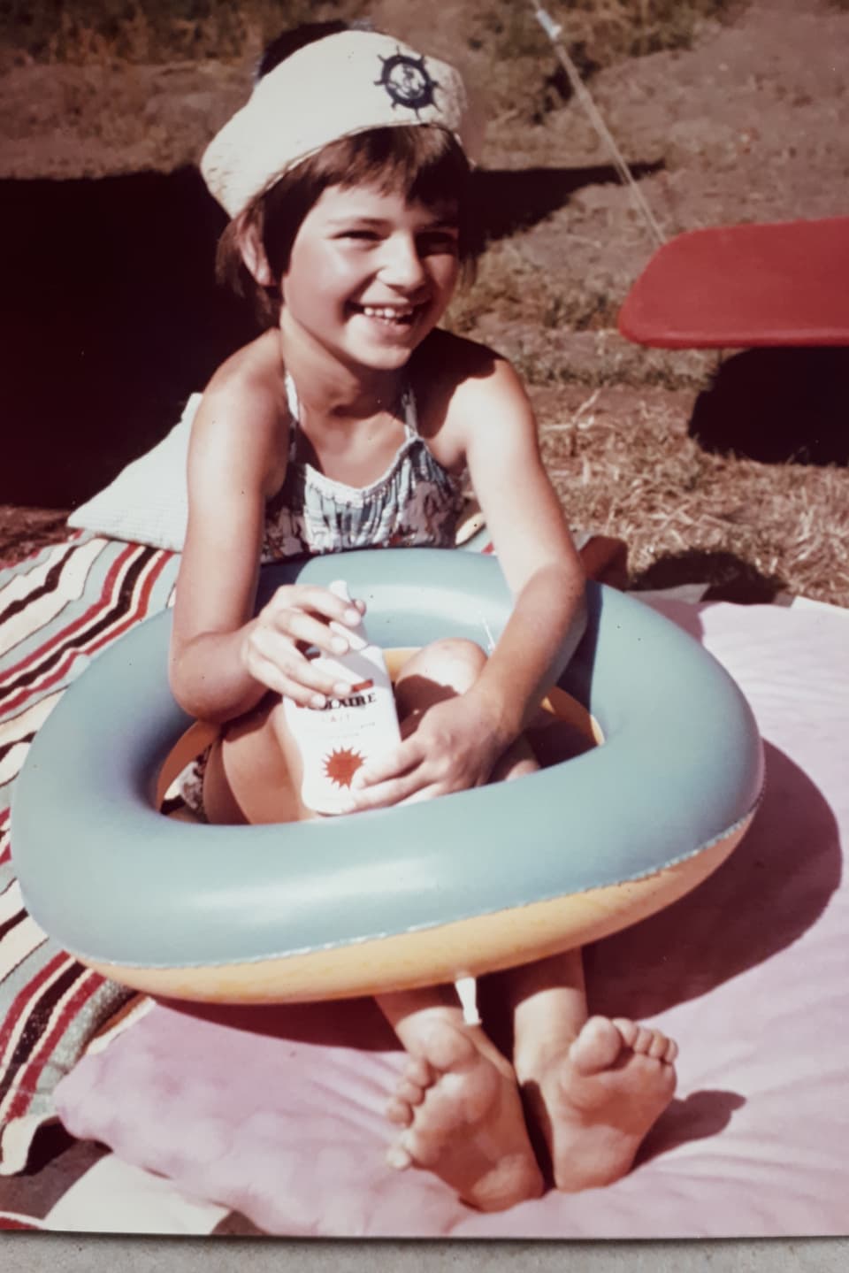 Ein Mädchen sitzt mit dem Schwimmring auf einem Badetuch.