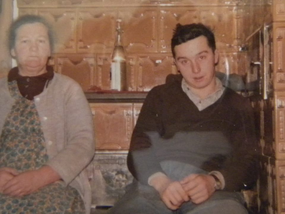Mutter und Sohn sitzen auf der Ofenbank eines Bauernhauses.