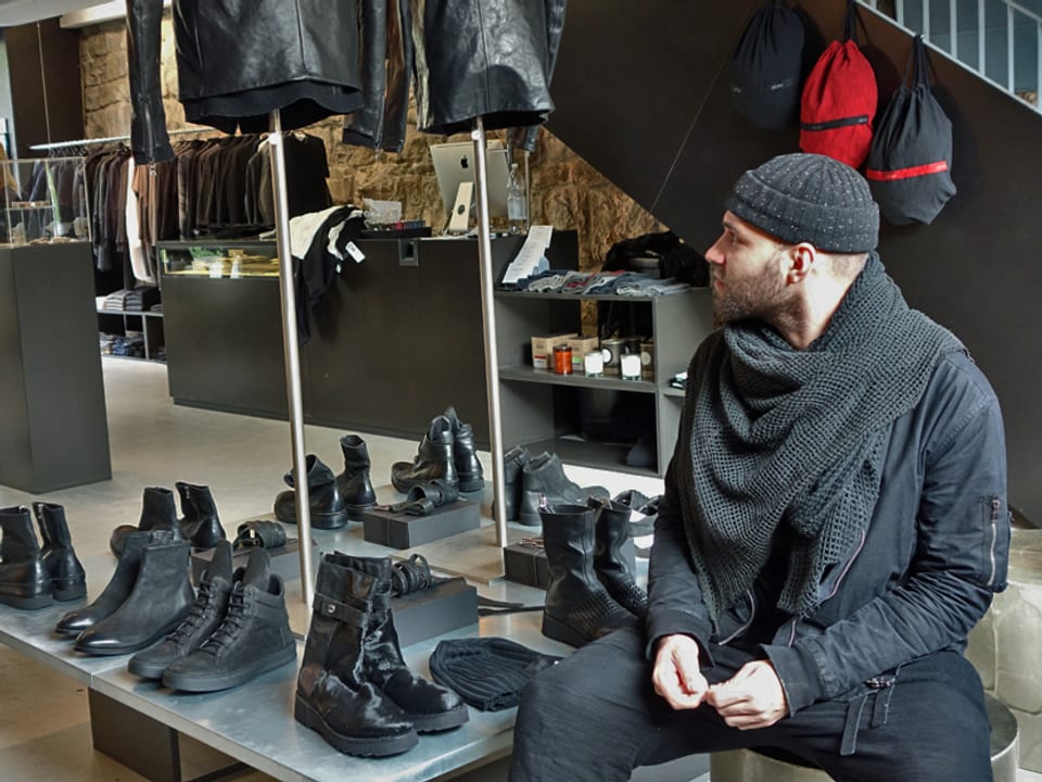 Der Designer sitzt in einer Boutique neben Schuhen und Jacken.
