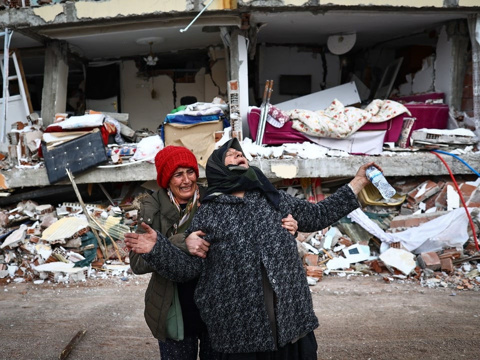 Zwei weinende Frauen vor einem kaputten Haus.