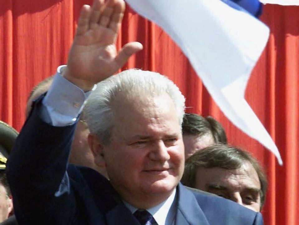 Slobodan Milošević winkend vor einer Fahne