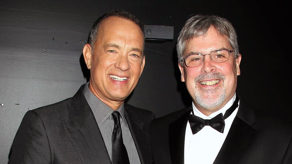 Tom Hanks und Richard Phillips (mit Brille), elegant gekleidet und in die Kamera lachend.