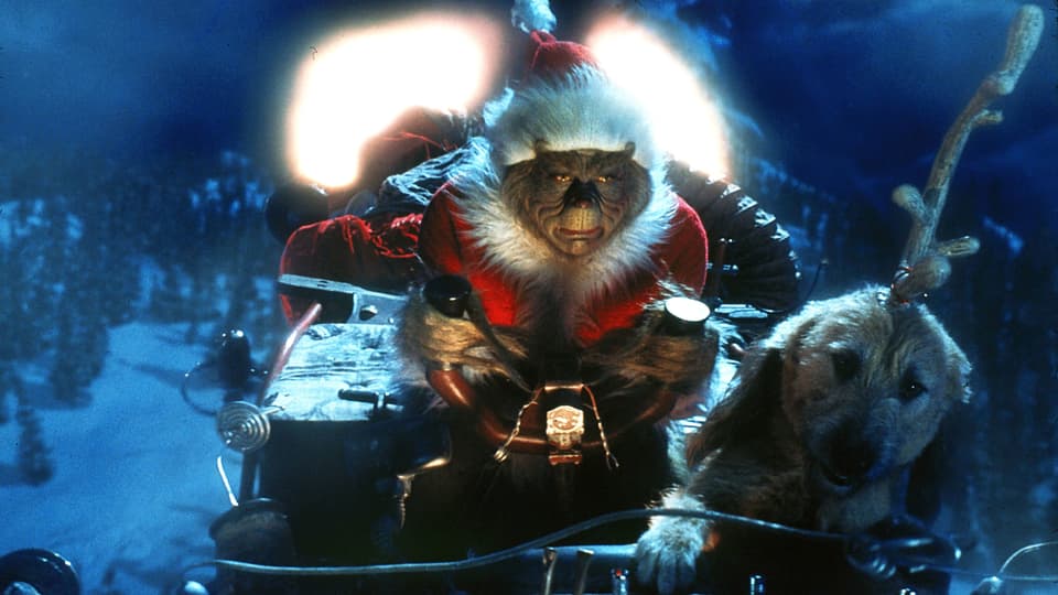 Szene aus dem Film "How The Grinch Stole Christmas": Ein haariges Monster in Samichlaus-Mütze und -Gewand rast in einem Schlitten über eine schneebedeckte Landschaft. Gezogen wird der Schlitten von einem kleinen Hund, dem ein Rentier-Geweih auf den Kopf gebunden wurde.