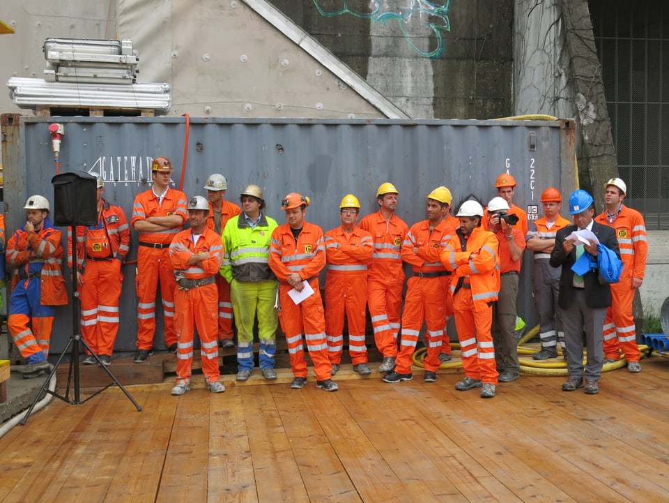 Eine Gruppe von Mineuren in orangen Arbeitskleidern wartet auf die Arbeit.