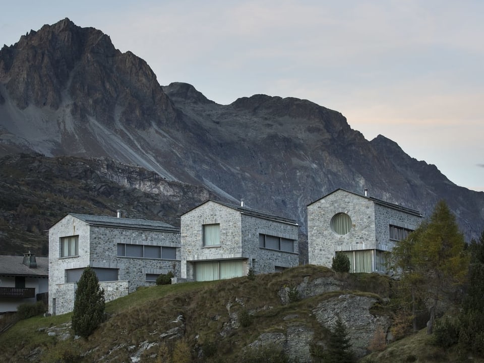 Drei moderne Häuser voer einer schriffen Felswand.