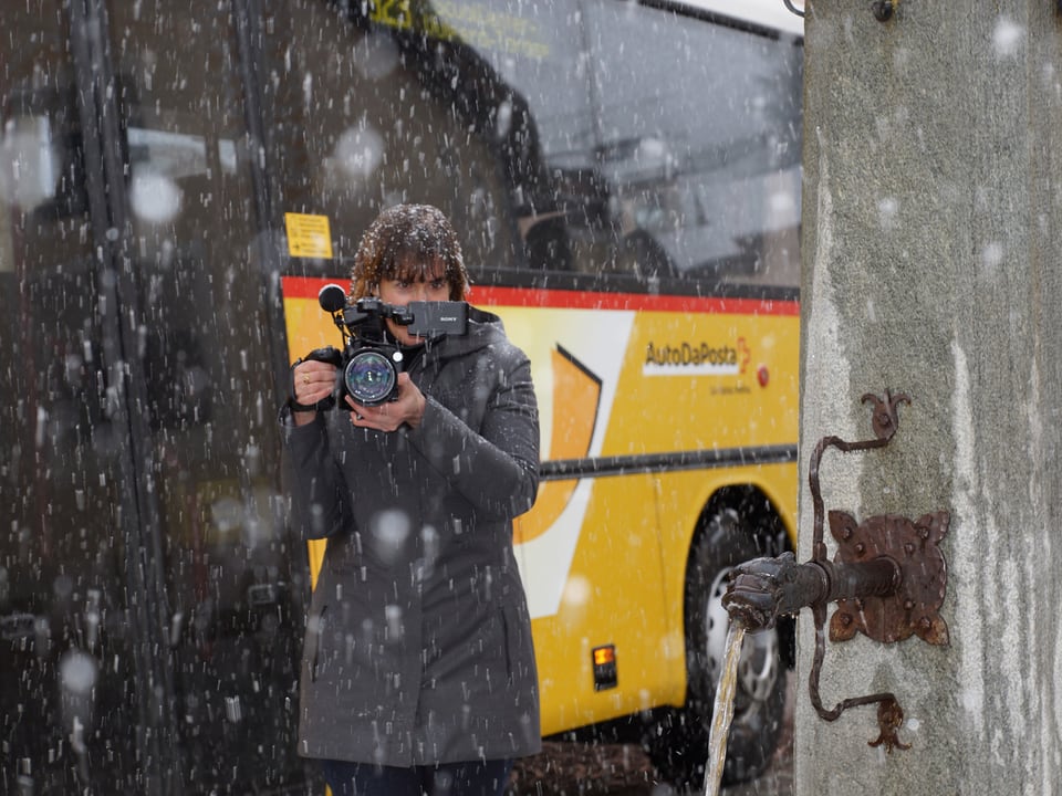 Eine Frau mit grosser Videokamera vor einem Postauto.