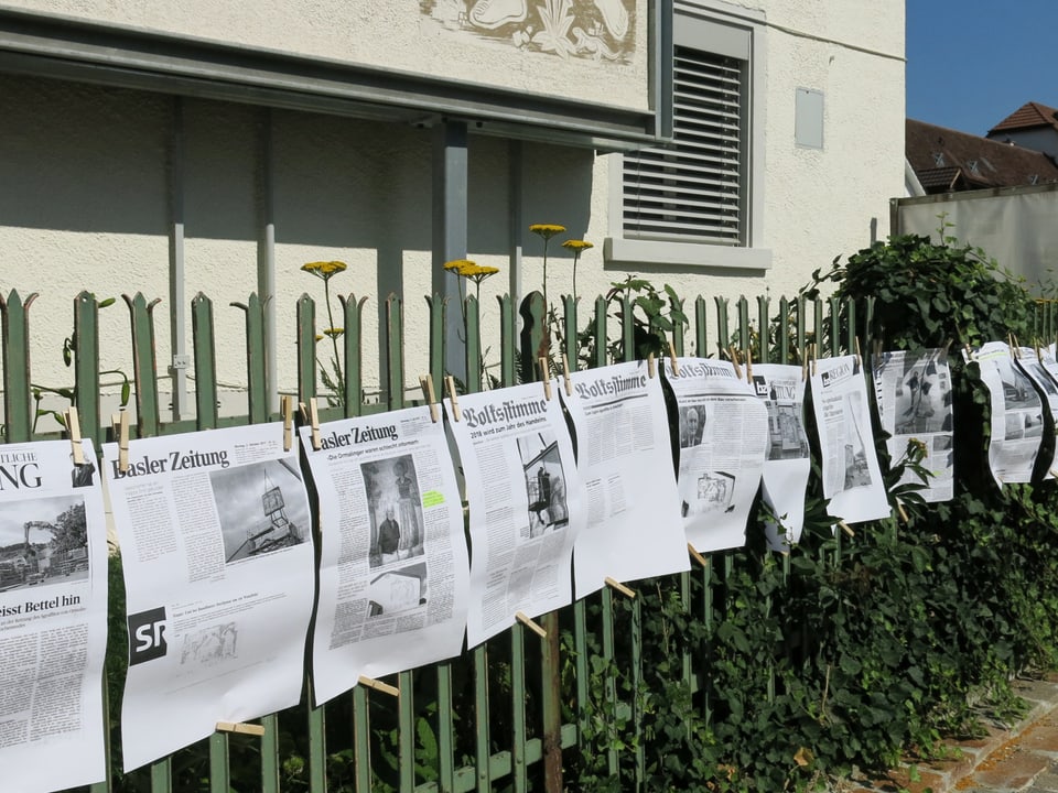 Zeitungsartikel hängen an einem Gartenzaun