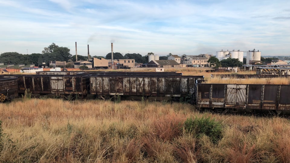Ein alter Zugwaggon steht auf einer dürren Wiese und verrottet.