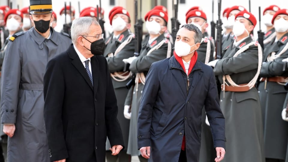 zwei Männer mit Maske schreiten Militärparade ab.