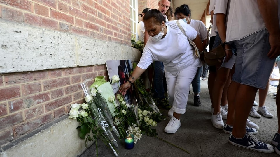 Eine Frau legt Blumen vor deinem Bild des verstorbenen Busfahrers nieder.