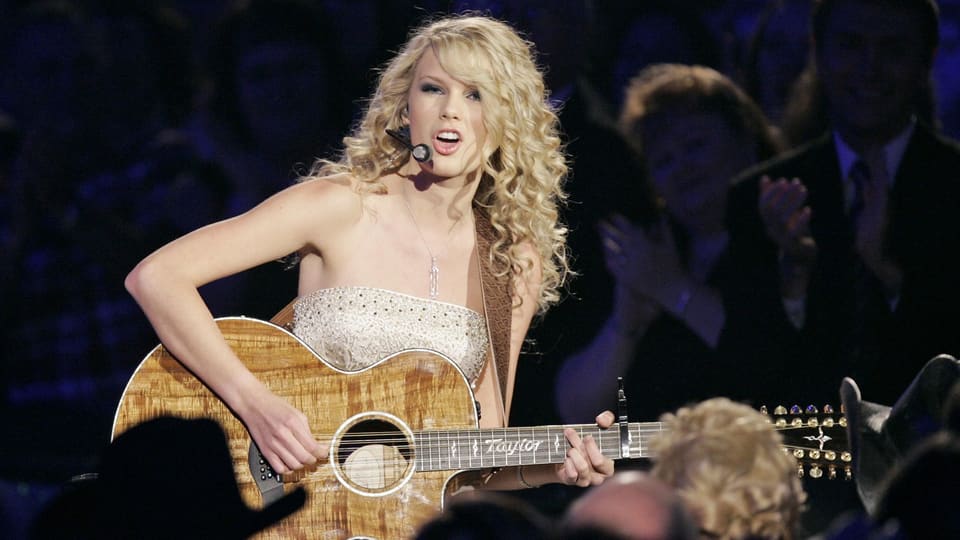 Blonde Sängerin spielt Gitarre auf einer Bühne vor Publikum