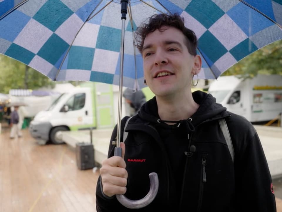 Ein Mann hält einen Regenschirm. Im Hintergrund ein Markt. Es regnet.