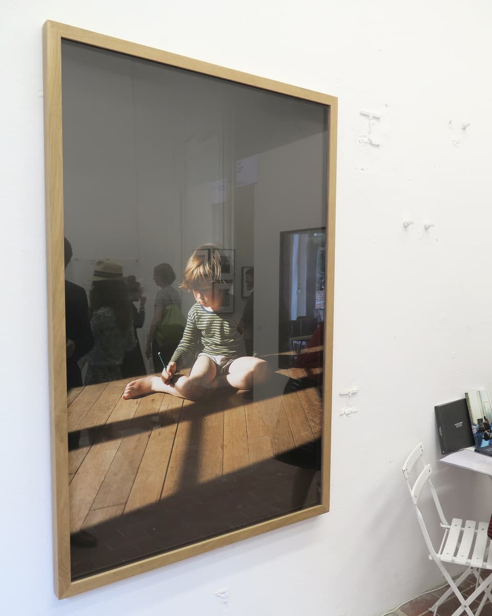 Ein Bild mit einem Bub drauf, im Glas spiegeln sich Besucher.