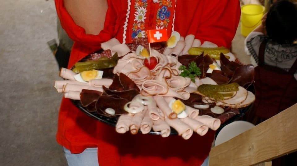 Fleischplatte mit Schweizer-Fähnchen dekoriert vor Edelweiss-Bluse. 