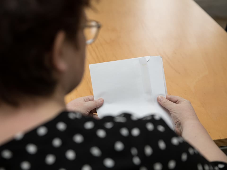 Eine Frau sitzt am Tisch und öffnet einen Brief.